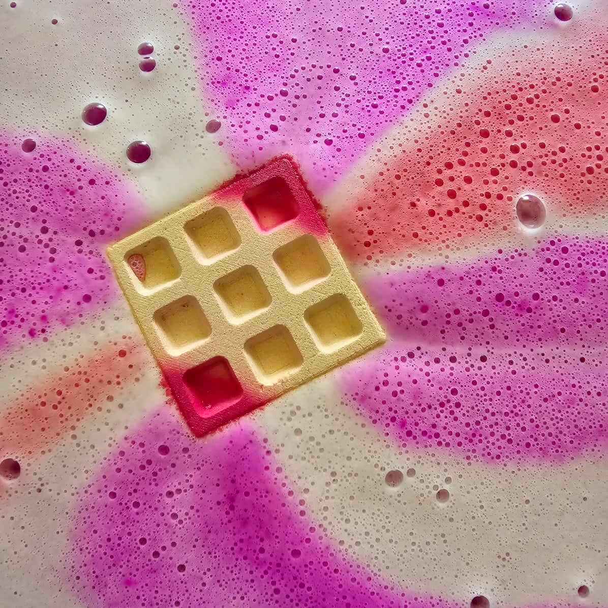 Bath bomb shaped like a waffle dissolving in bath water