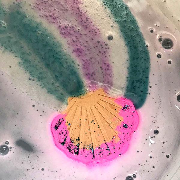 Mermaid Cove Bath Bomb in action: pink and gold clam shell bath bomb fizzing in a bathtub filled with water, creating a magical and relaxing mermaid experience